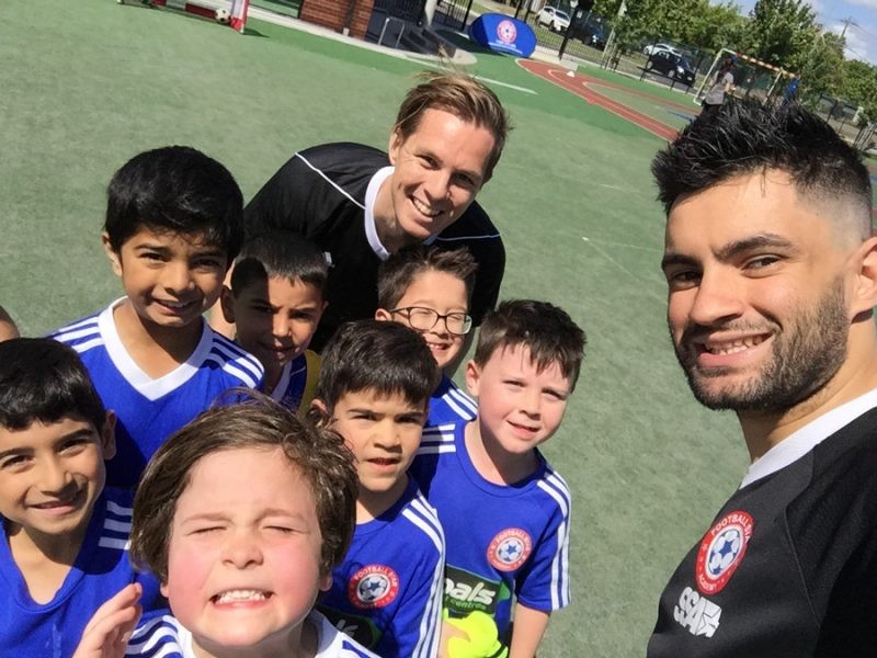 estudiante Dani con su equipo de niños pequeños de fútbol y otro entrenador sonriendo y con el uniforme azul